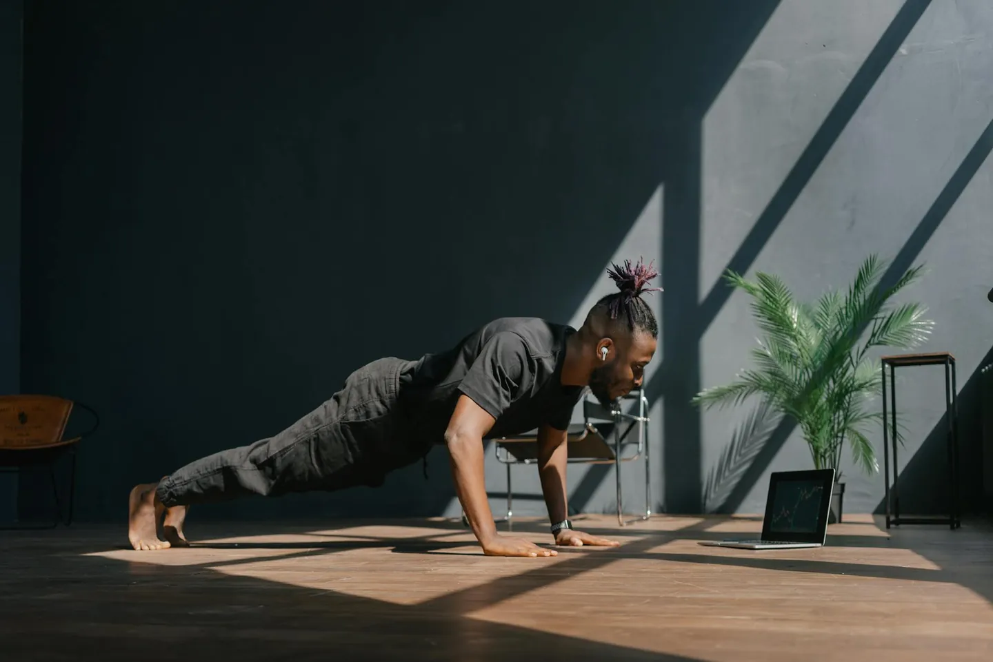 Man doing push-ups at home beside a laptop, representing a no-equipment bodyweight HIIT workout.
