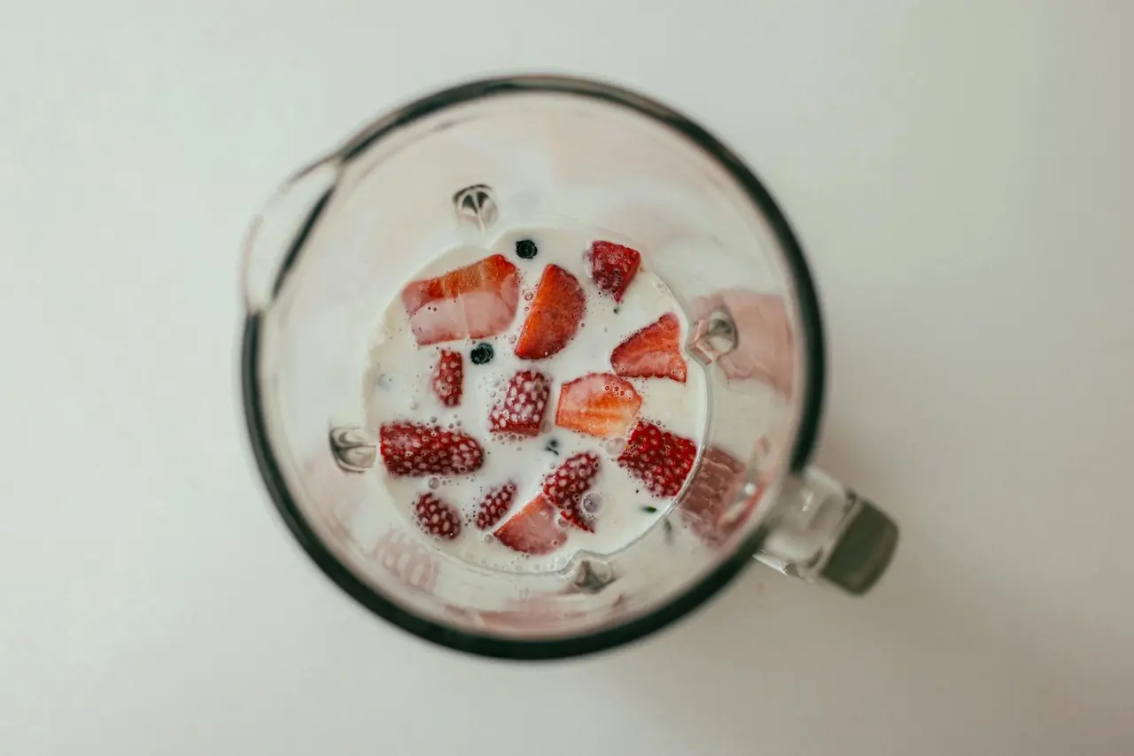 Strawberries and milk in a blender viewed from above, representing a blender for smoothies and meal prep.