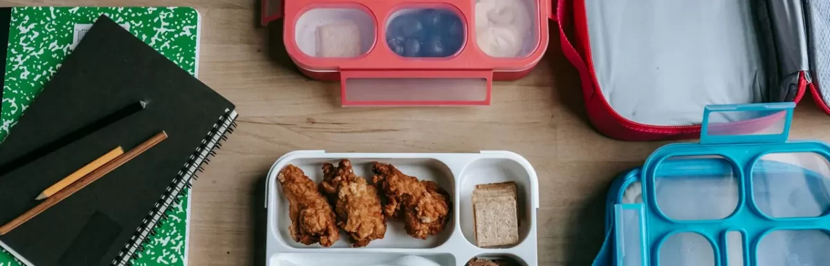 Healthy lunchboxes with fruit and chicken on a wooden desk, representing simple meal prep.