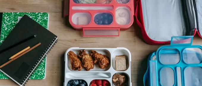 Healthy lunchboxes with fruit and chicken on a wooden desk, representing simple meal prep.