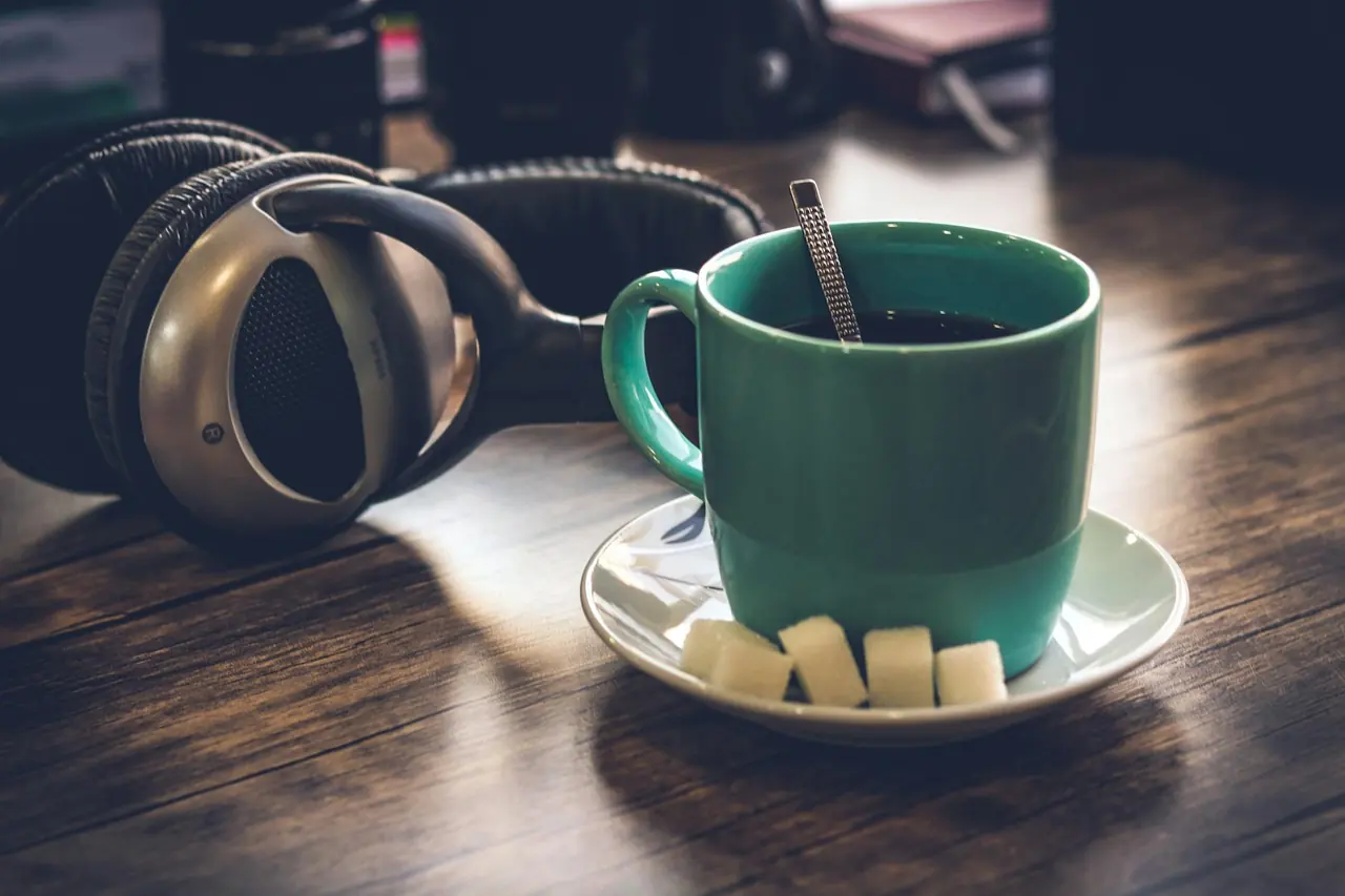 Green coffee cup with sugar cubes and headphones on a wooden table.