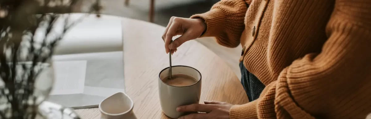 Woman stirring coffee at home in the morning, representing a first cup of coffee before breakfast.