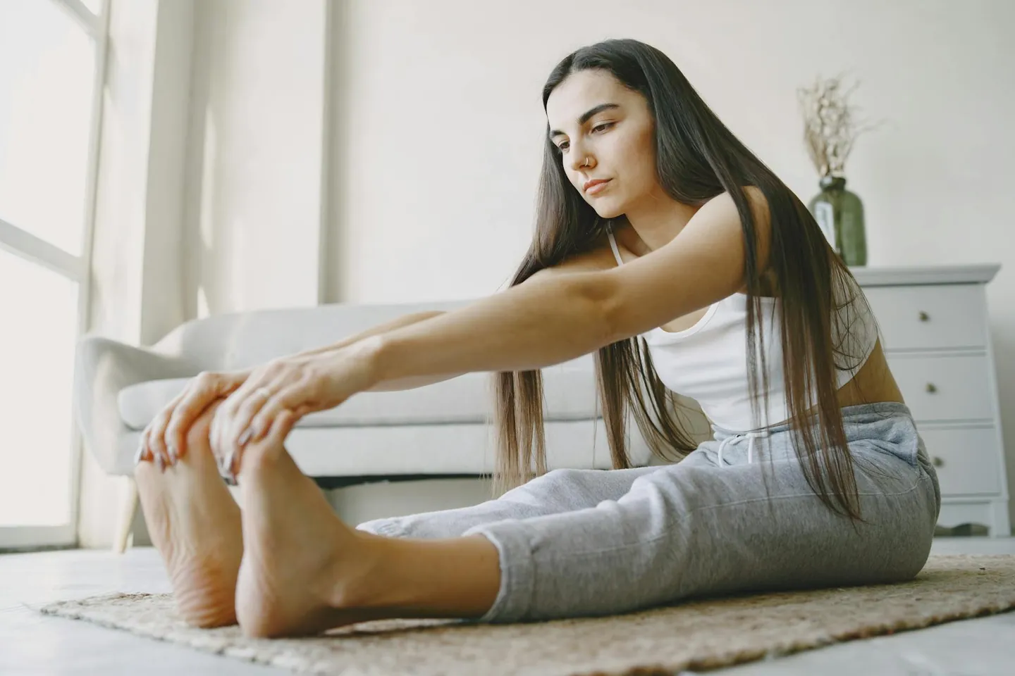 Woman stretching on a rug in a bright room after exercise, representing a cooldown after a HIIT workout.
