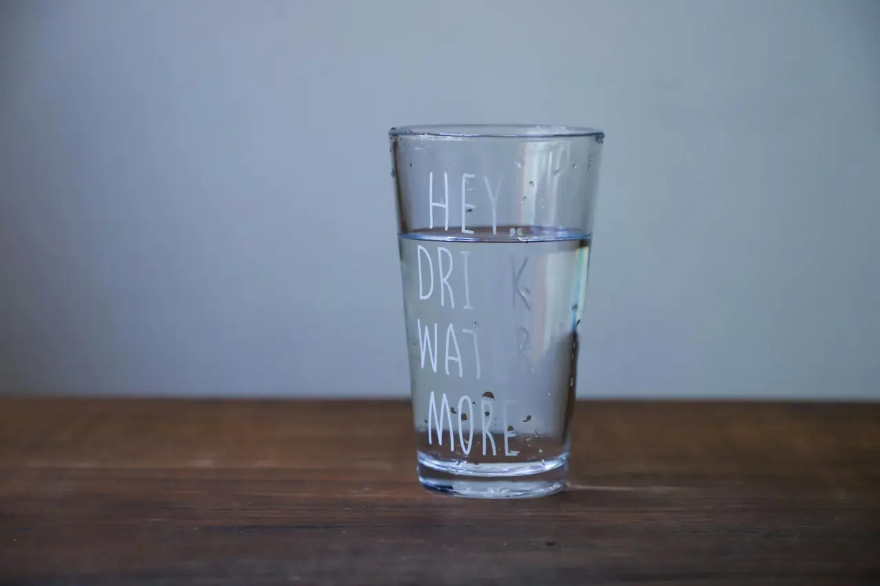Glass of water on a table with a message reminding people to drink more water.