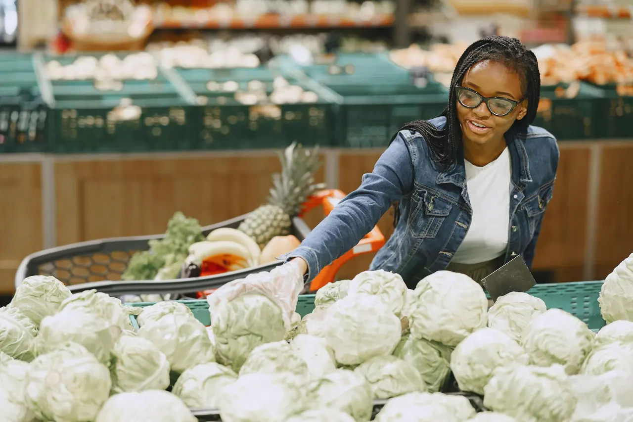 Woman selecting fresh cabbage in a grocery market, representing healthy grocery shopping on a budget.