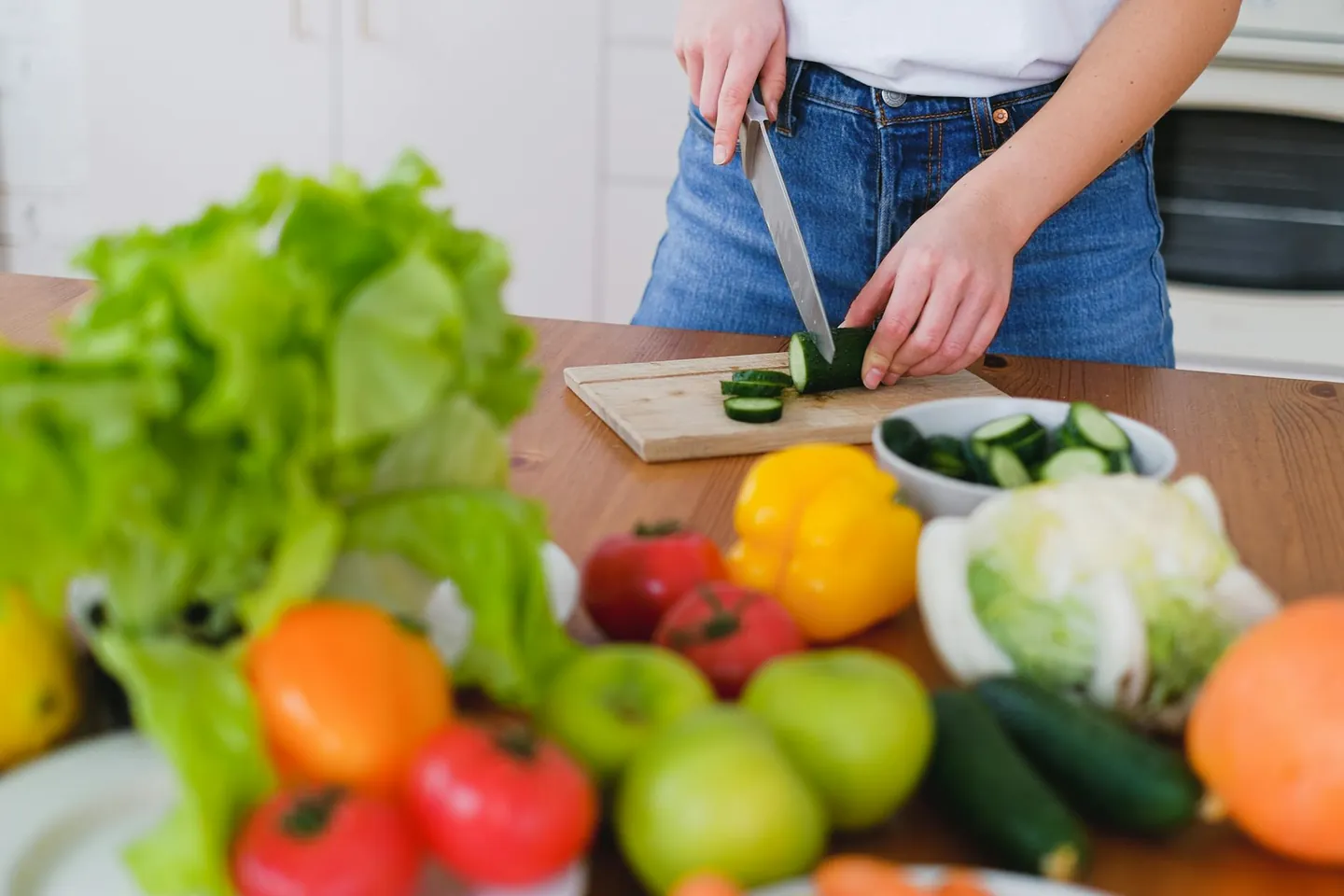Woman preparing fresh vegetables in a bright kitchen, representing healthy meal prep and nutrition.