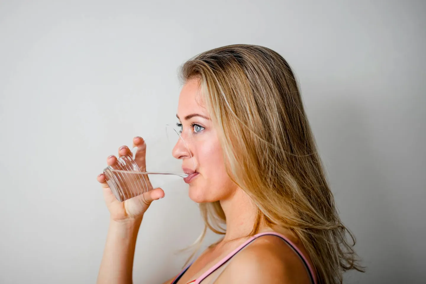 Woman drinking a glass of water, representing hydration and healthy daily habits.