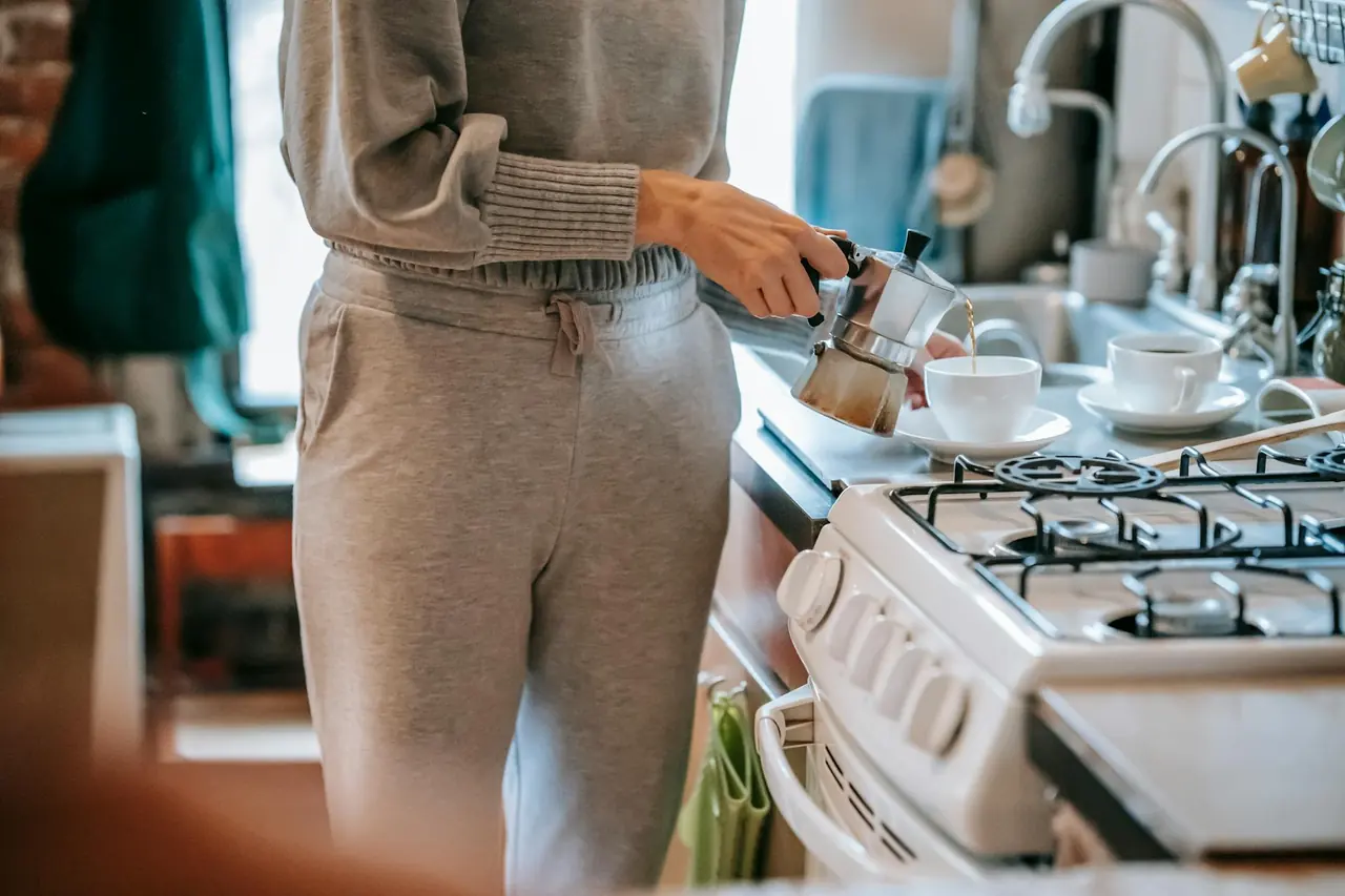 Woman pouring freshly brewed coffee from a moka pot in a kitchen.