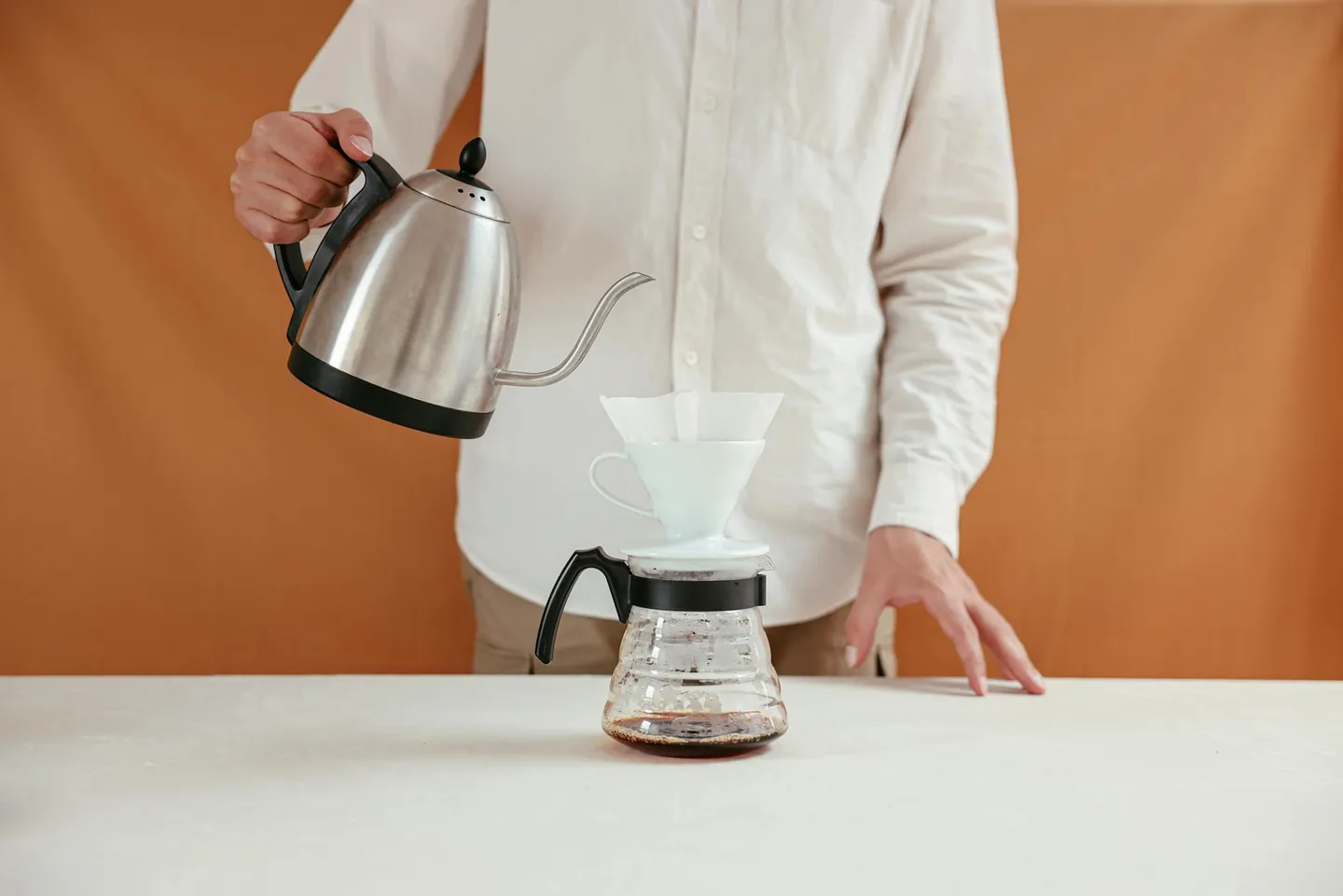 Person making pour over coffee with a dripper and kettle at home.