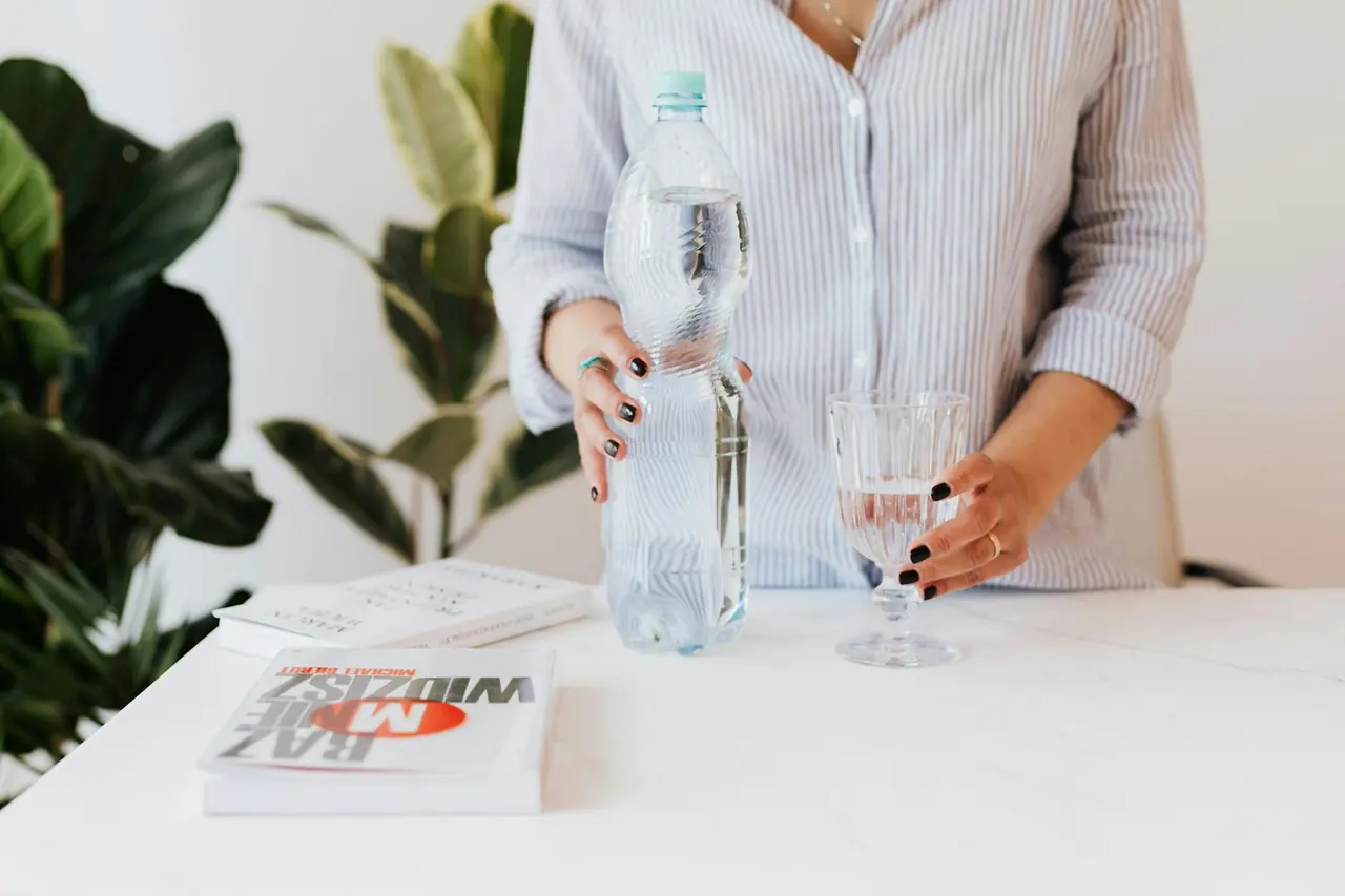 Woman pouring water into a glass beside books, representing a simple hydration routine at home.