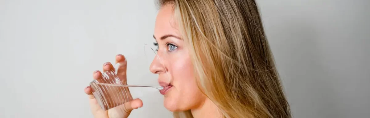Woman drinking water from a clear glass, representing healthy hydration habits.