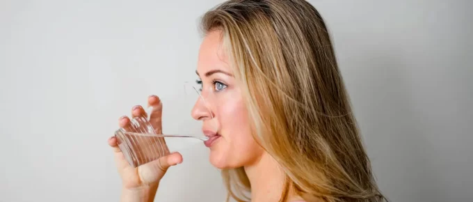 Woman drinking water from a clear glass, representing healthy hydration habits.