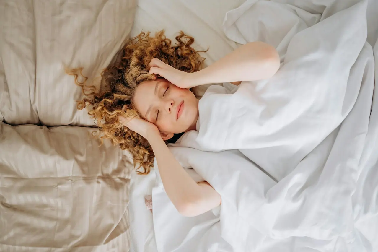 Woman sleeping peacefully under white sheets, representing sleep and recovery.