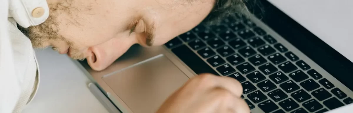 Exhausted employee resting head on laptop keyboard, representing fatigue and burnout.