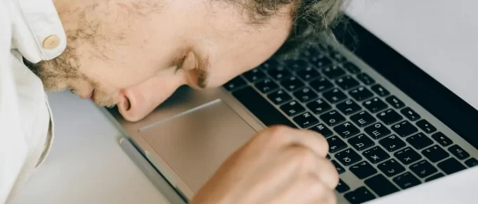 Exhausted employee resting head on laptop keyboard, representing fatigue and burnout.