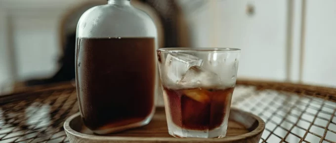 Glass of cold brew coffee with ice beside a bottle