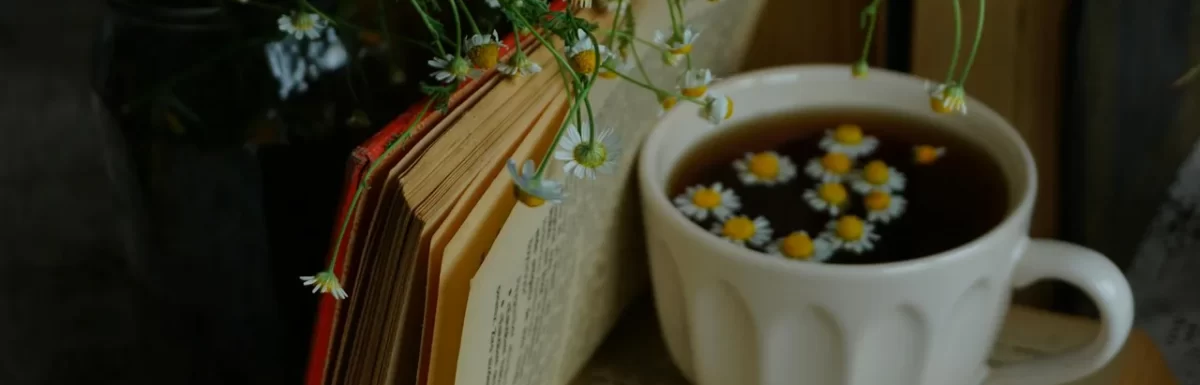 Cup of herbal tea on a bedside table beside a book and warm lamp