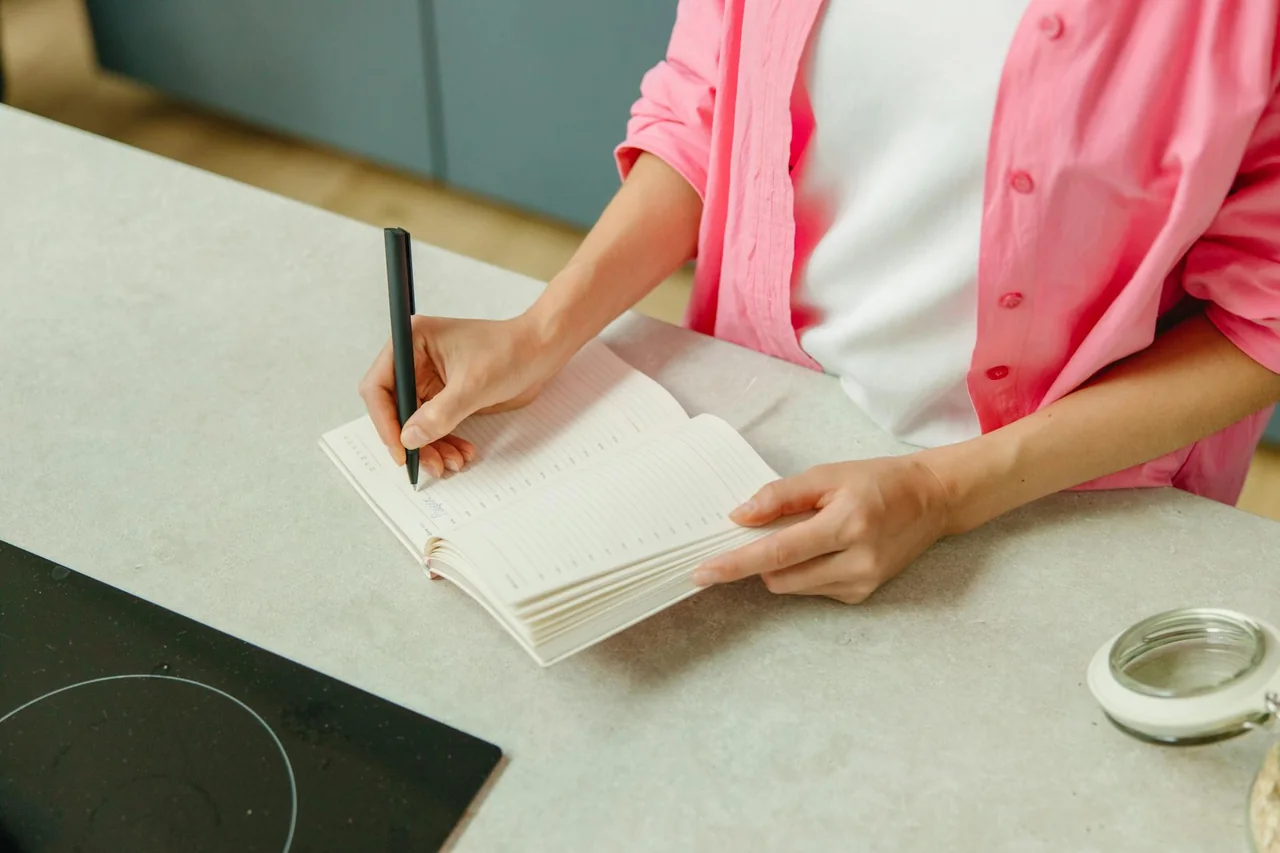 Handwritten grocery list and pen on a kitchen table