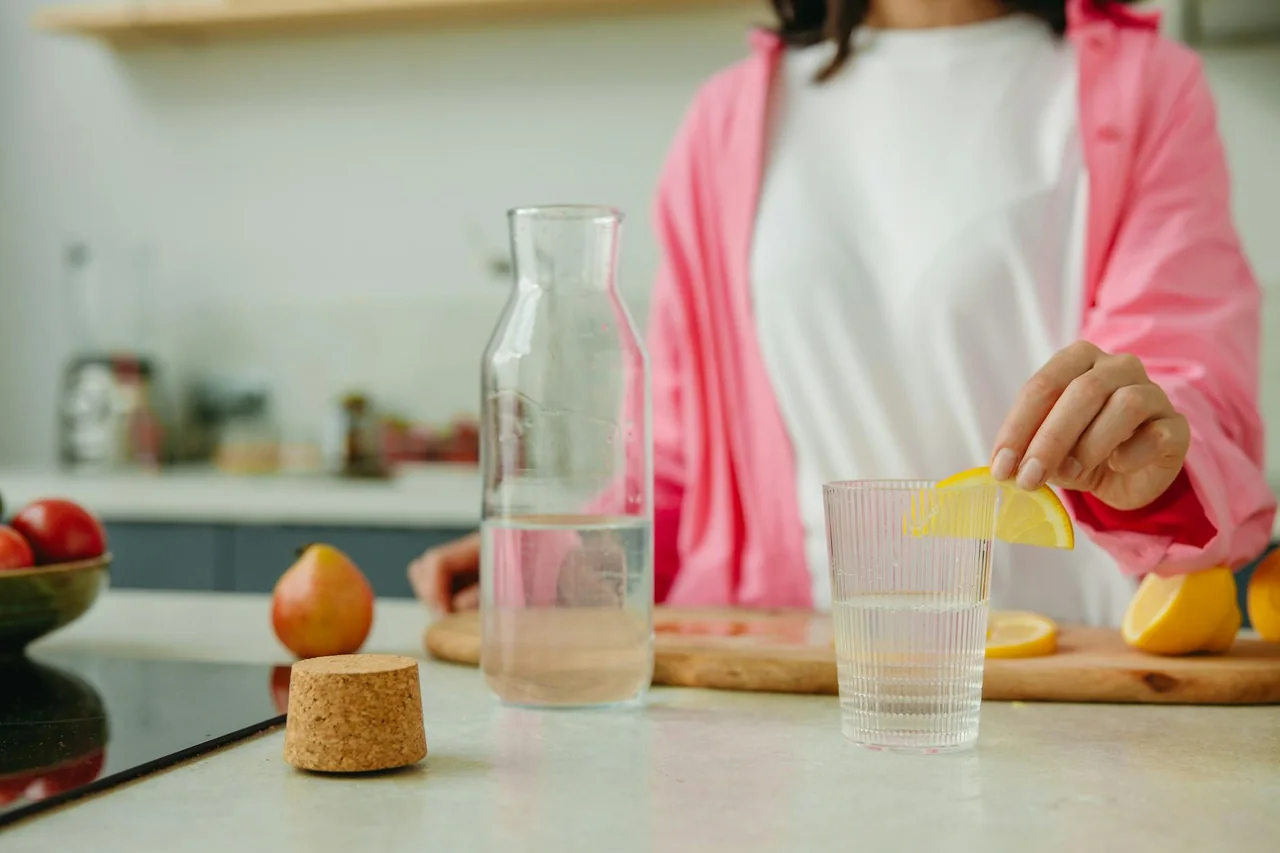 Person drinking water in the kitchen during the evening