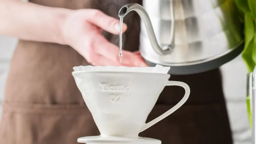 A gooseneck kettle pouring water into a ceramic coffee dripper.