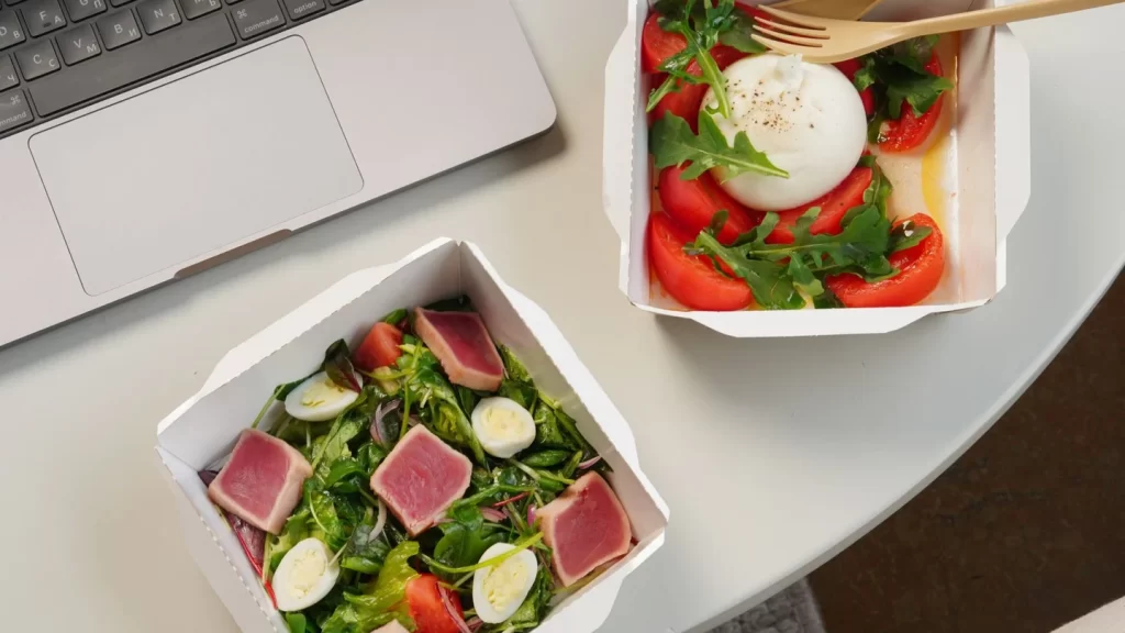 Two salad containers beside a laptop, including a salad topped with a boiled egg.