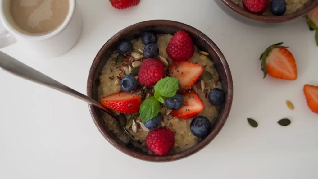 A breakfast bowl topped with berries and banana, beside a cup of coffee.